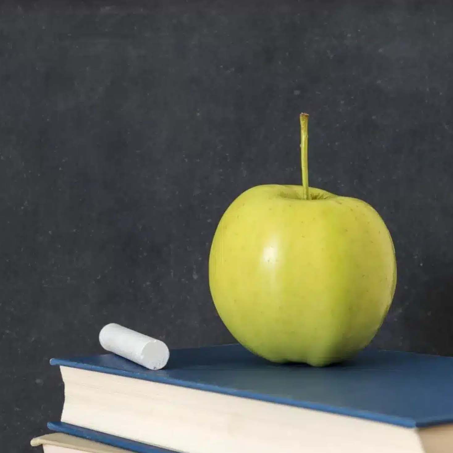 A Stack of Books with Chalks and Apple on top of it with Chalkboard background