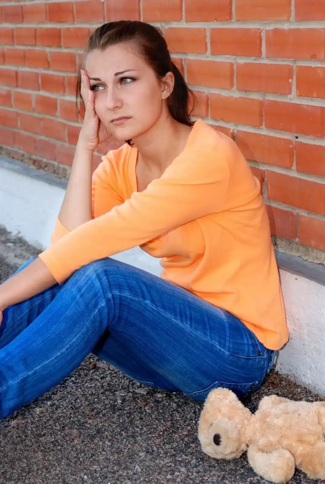 Sad girl sitting on ground and leaning on block getting bullied