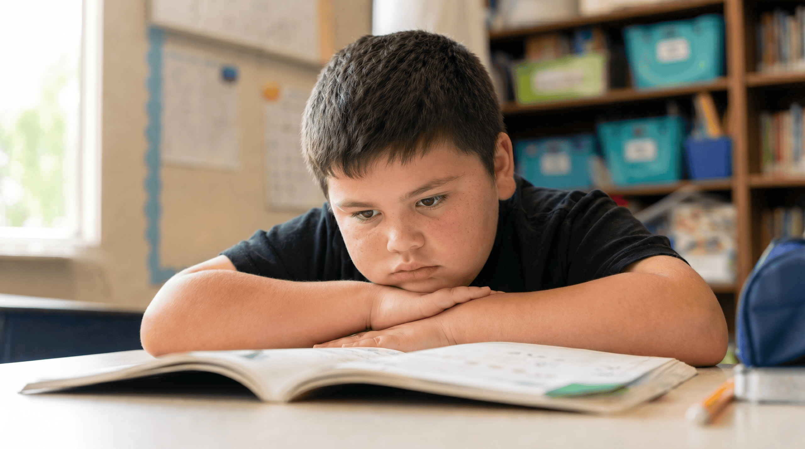 Child with special needs smiling while working on schoolwork at a desk with a supportive tutor nearby