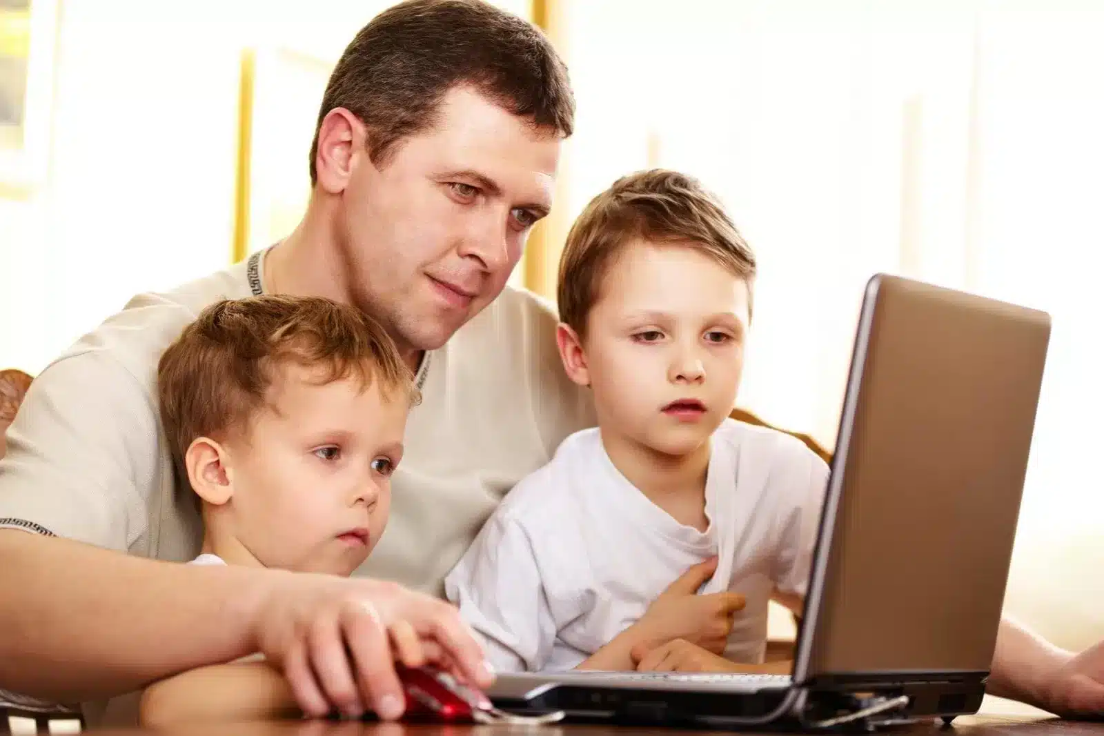 A Father teaching his two sons how to operate a laptop