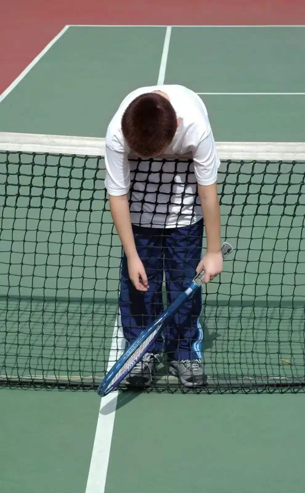 Boy hunched over tennis net